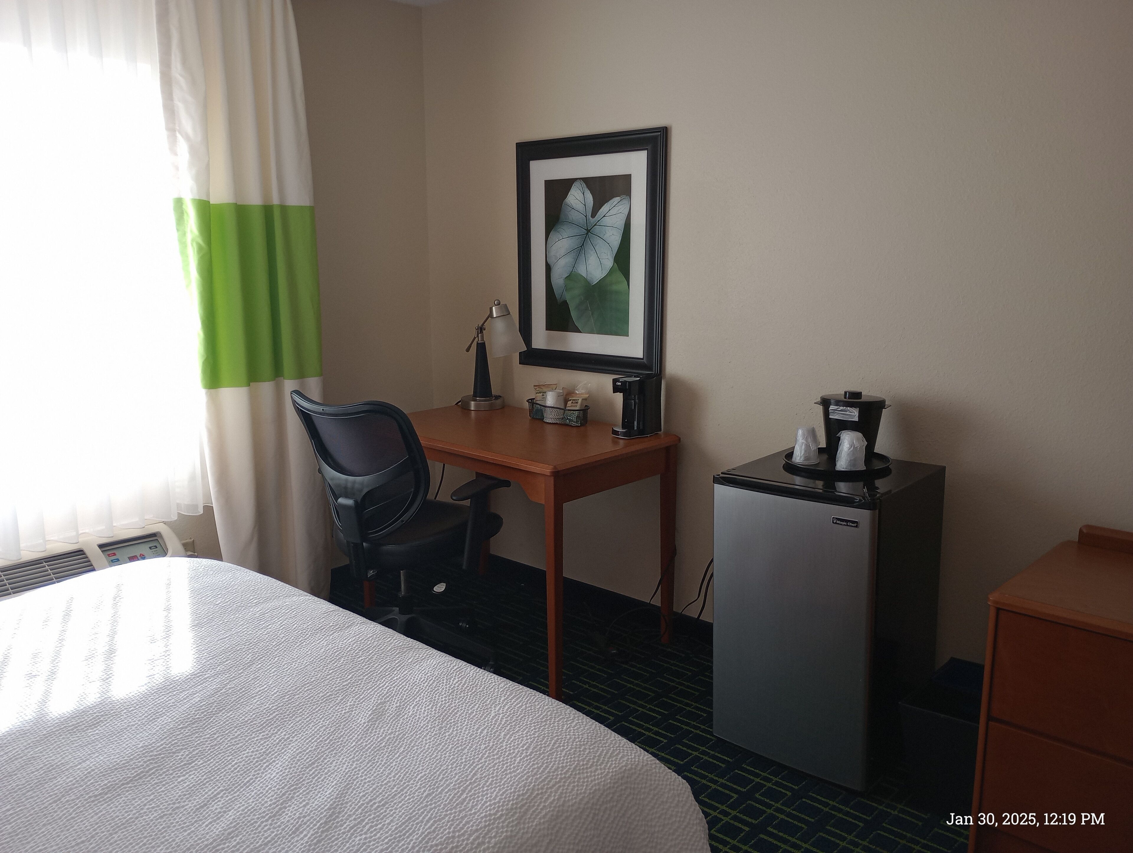 Une chambre d’hôtel équipée d’un lit, d’un bureau, d’une chaise, d’une machine à café, d’un réfrigérateur et d’un tableau encadré au mur.