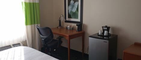 Une chambre d’hôtel équipée d’un lit, d’un bureau, d’une chaise, d’une machine à café, d’un réfrigérateur et d’un tableau encadré au mur.