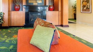 A hotel lobby with a sofa, two red vases, a fireplace, and a framed picture on the wall.