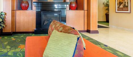 A hotel lobby with a sofa, two red vases, a fireplace, and a framed picture on the wall.