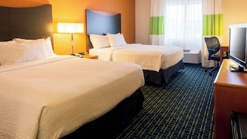 Una habitación de hotel con dos camas, un escritorio con televisor, una silla y una ventana con cortinas.