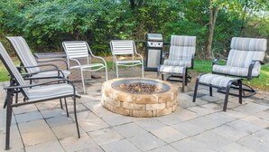An outdoor patio with four striped lounge chairs, a stone fire pit, and a grill.