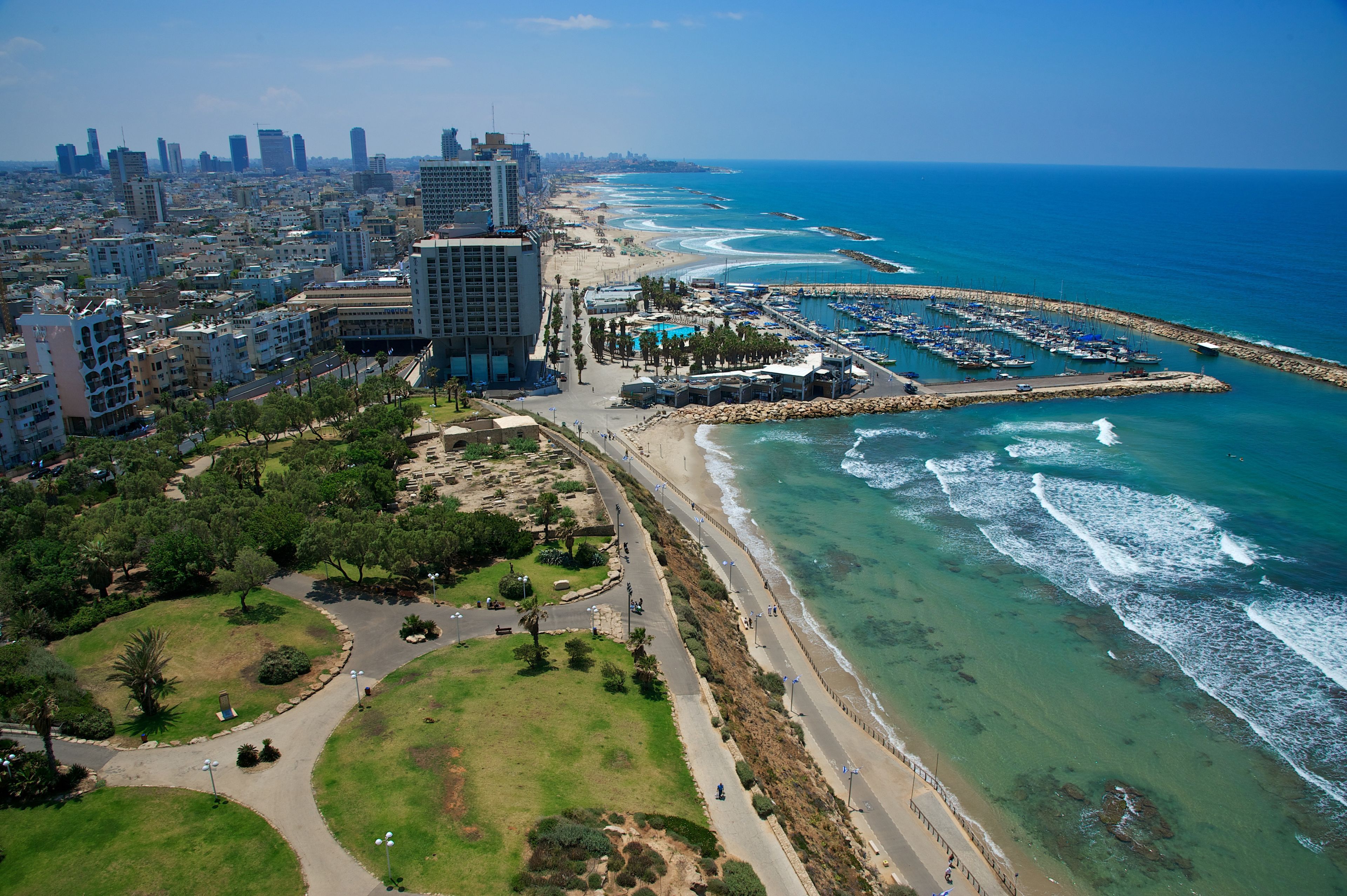 An aerial view of a coastal city with a marina, beachfront promenade, and dense urban buildings.