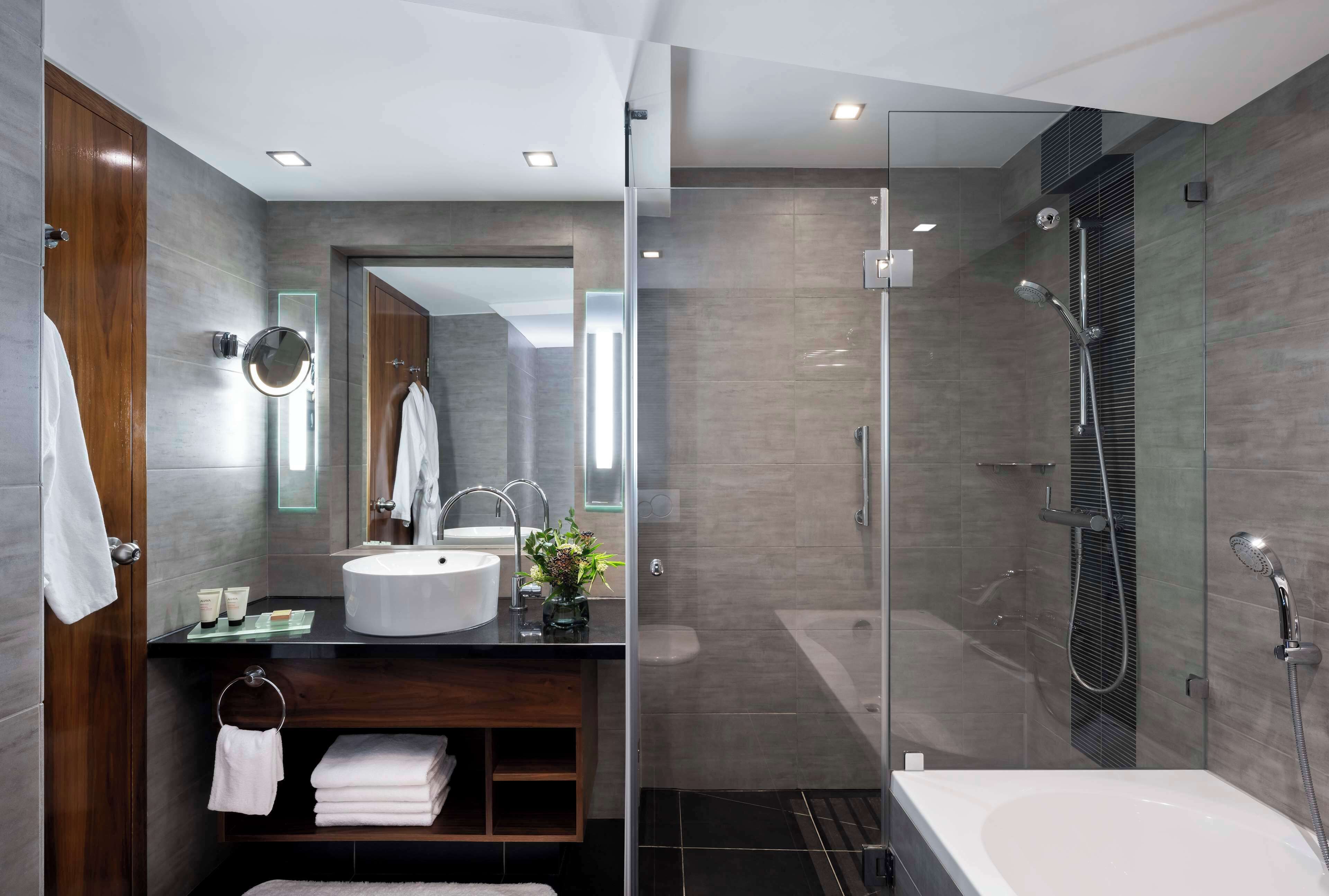 Une salle de bain moderne dotée d’un grand lavabo, d’un miroir et d’une douche à parois de verre.