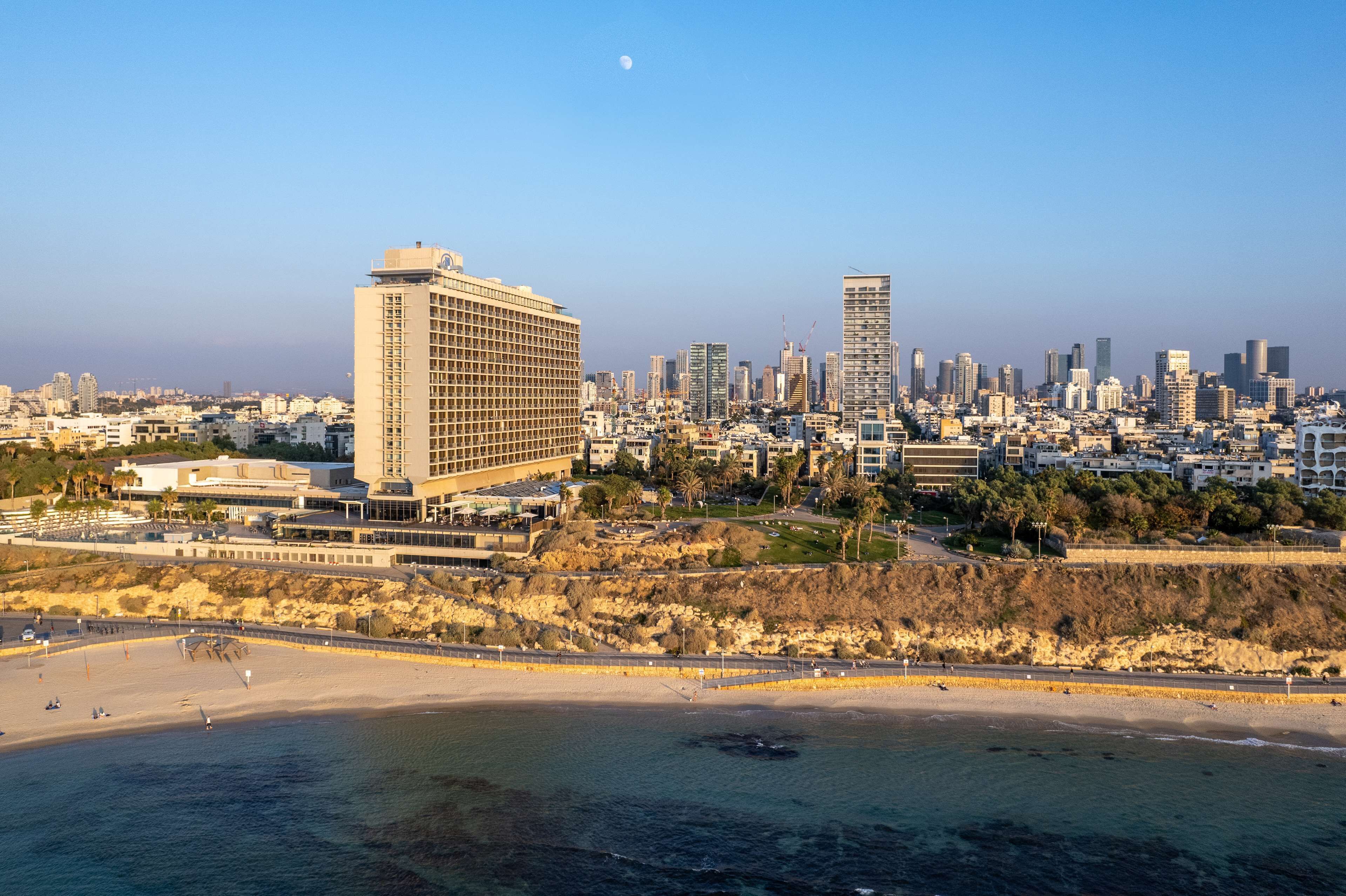 Un paisaje urbano costero con un hotel destacado que presenta una fachada en forma de cuadrícula, ubicado cerca de una playa arenosa y con vistas al océano.