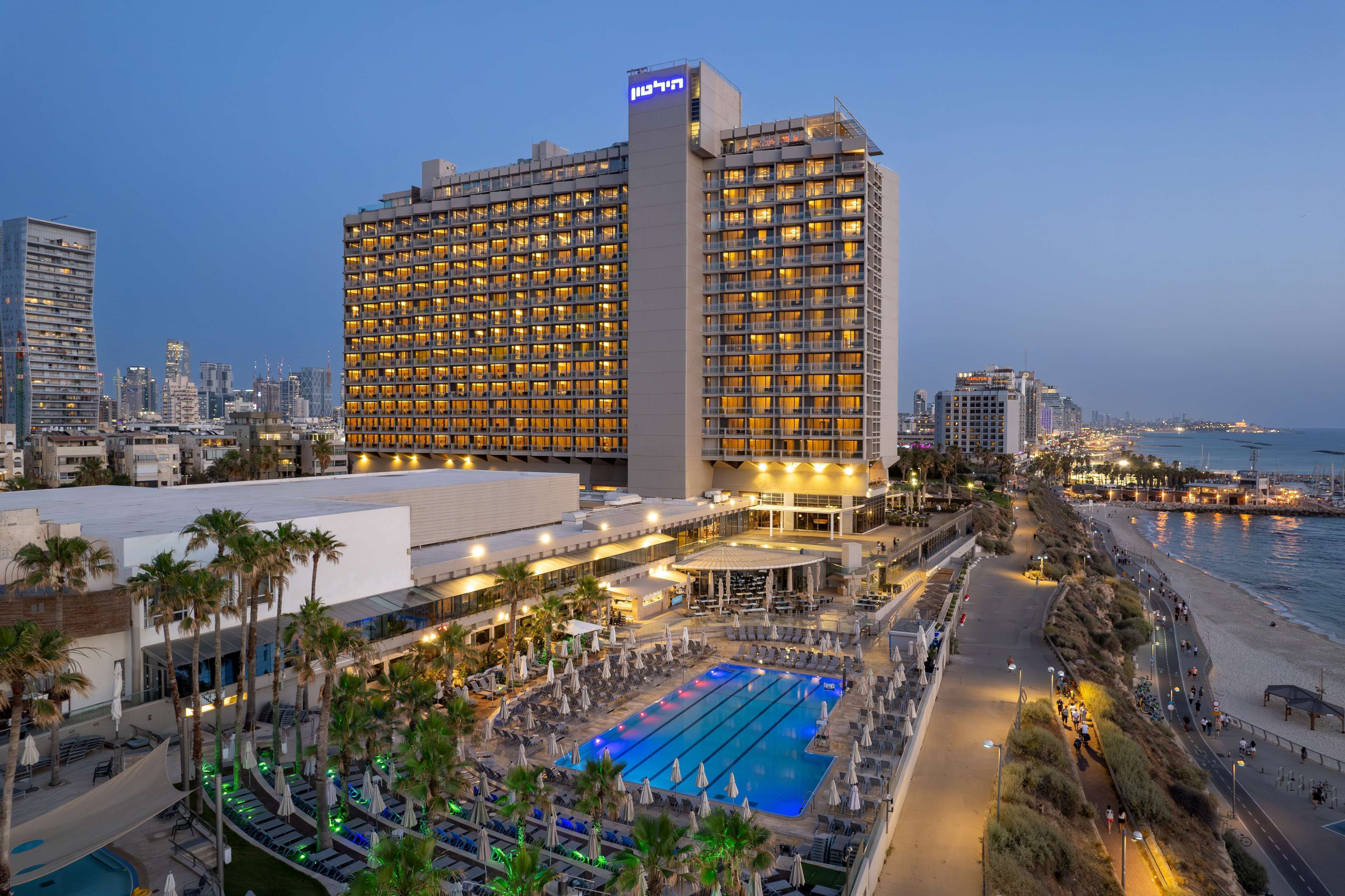 A hotel with a large pool, palm trees, and a view of the city skyline.