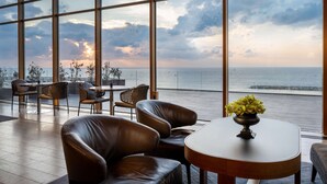 A modern interior with large windows, leather seating, and a table with a vase of flowers. - Hilton Tel Aviv (Tel Aviv)