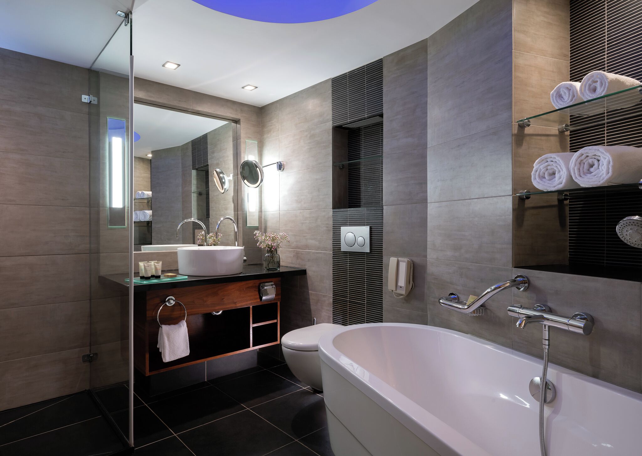 A modern bathroom with a glass shower enclosure, a freestanding bathtub, and a vanity with a mirror.