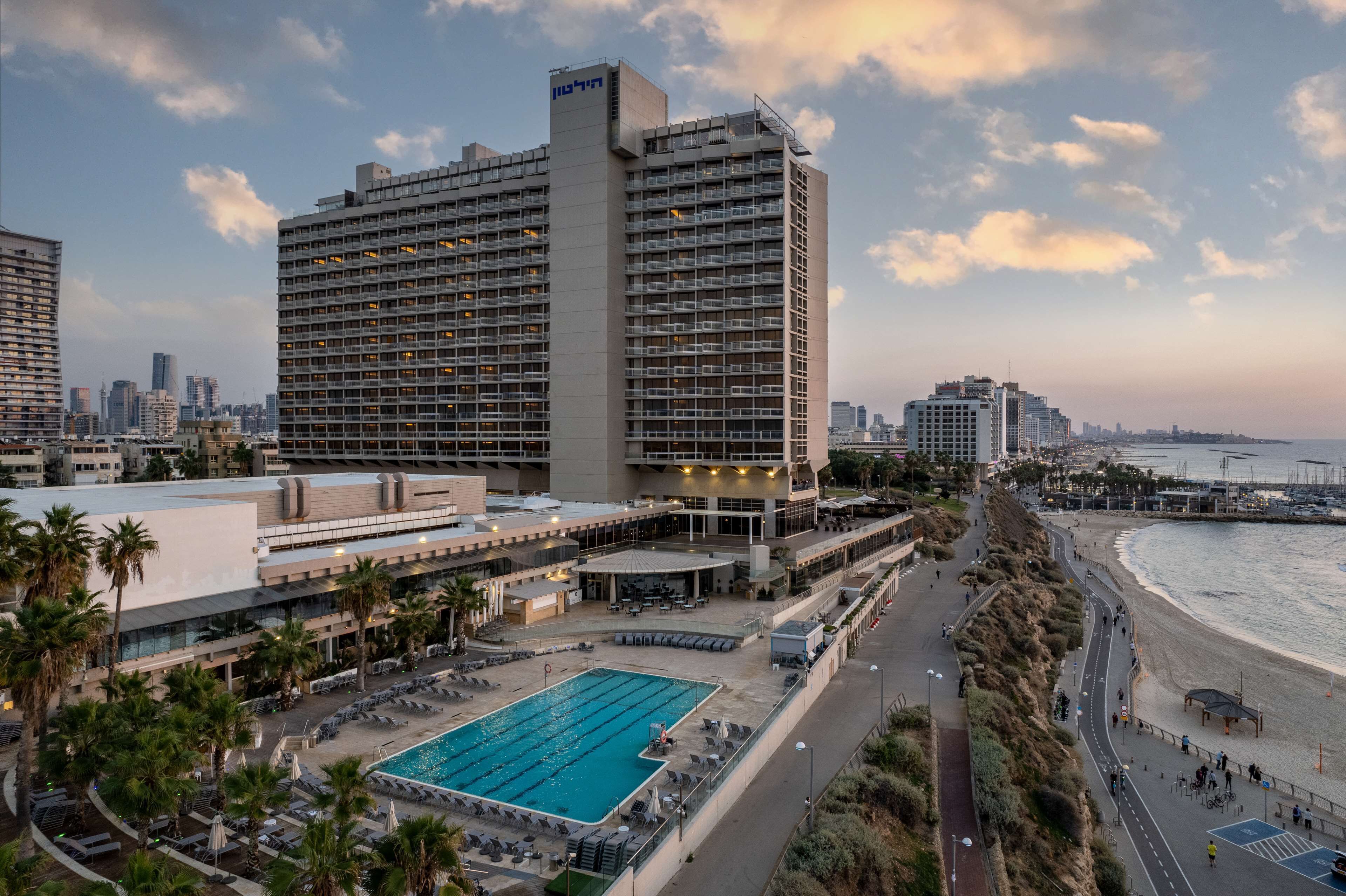 Un hotel amb una piscina gran, un passeig marítim i vista al perfil urbà de la ciutat.