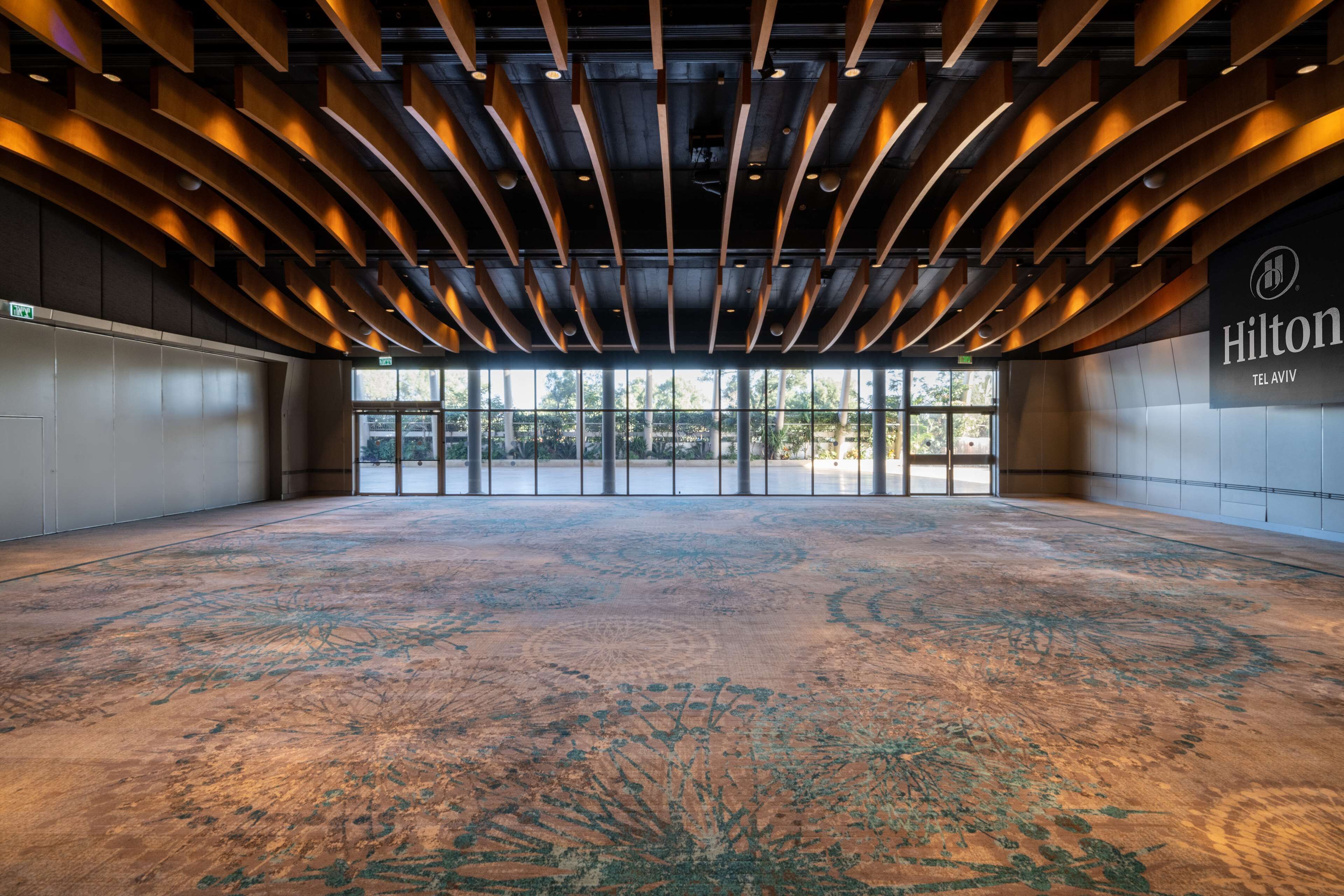 A spacious lobby with a large patterned carpet, a modern ceiling design, and large windows offering a view outside.