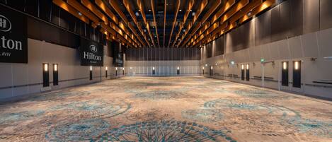 A spacious hotel lobby with a large carpeted area, wooden ceiling beams, and illuminated wall signs.