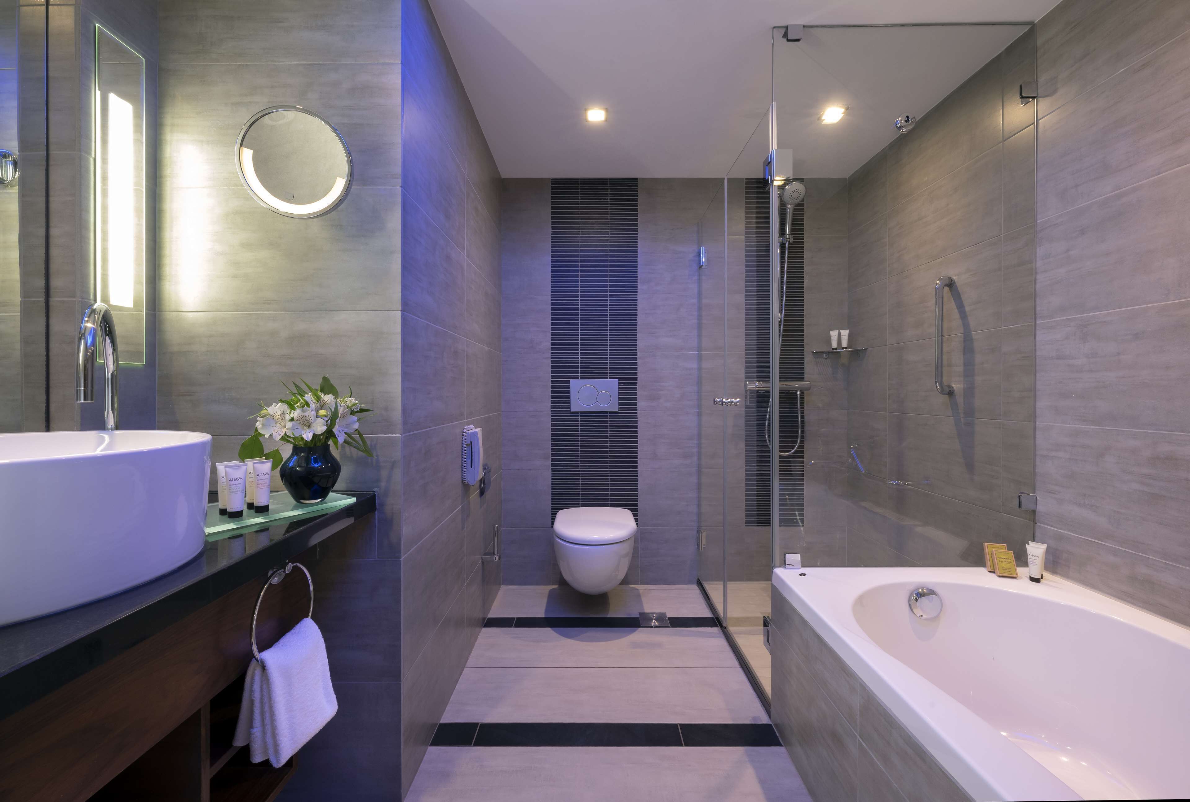 A modern bathroom with a large bathtub, a round mirror, and a toilet.