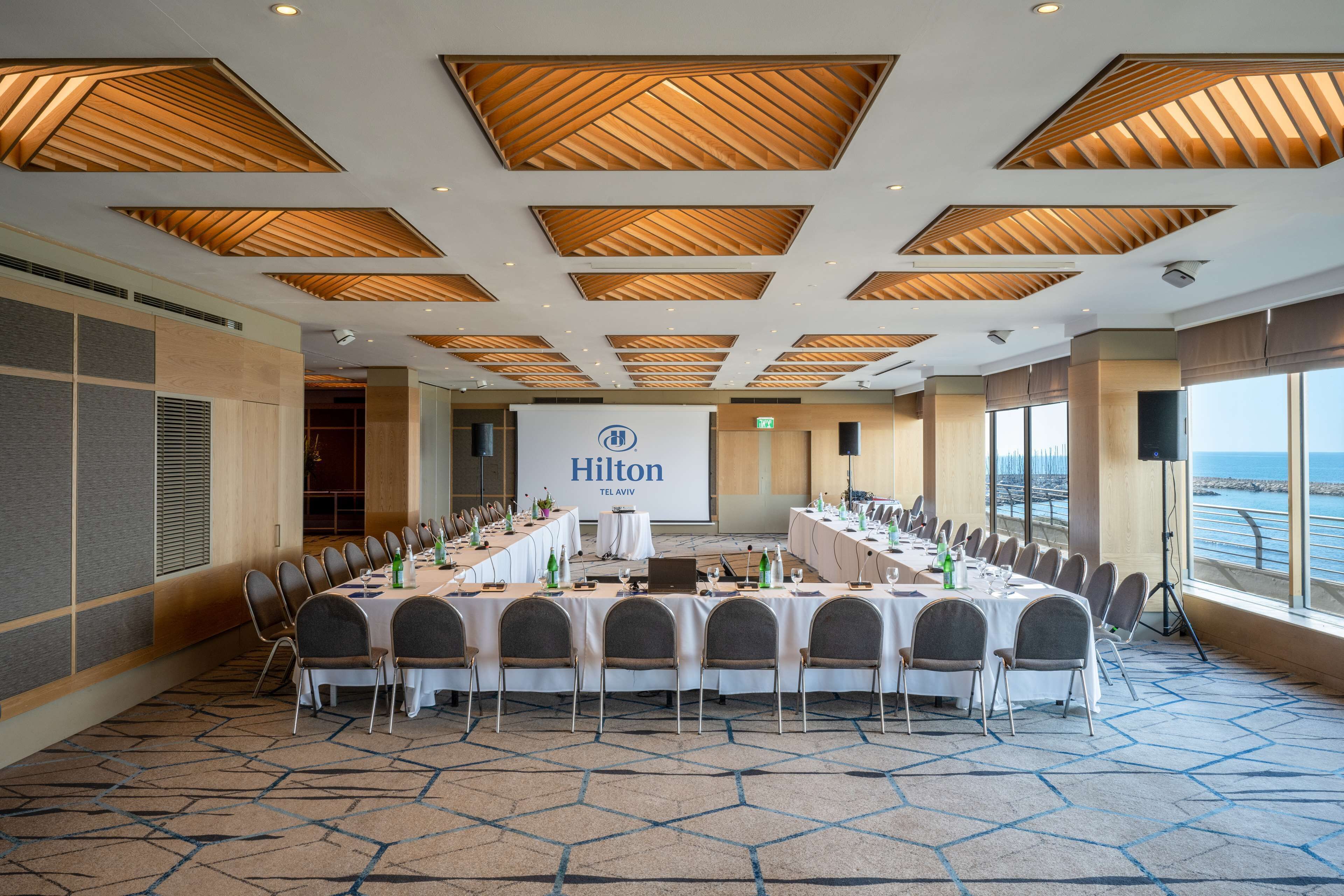 A conference room with a long table, chairs, and a large screen displaying 'Hilton'.