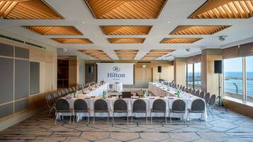 A conference room with a long table, chairs, and a large screen displaying 'Hilton'.