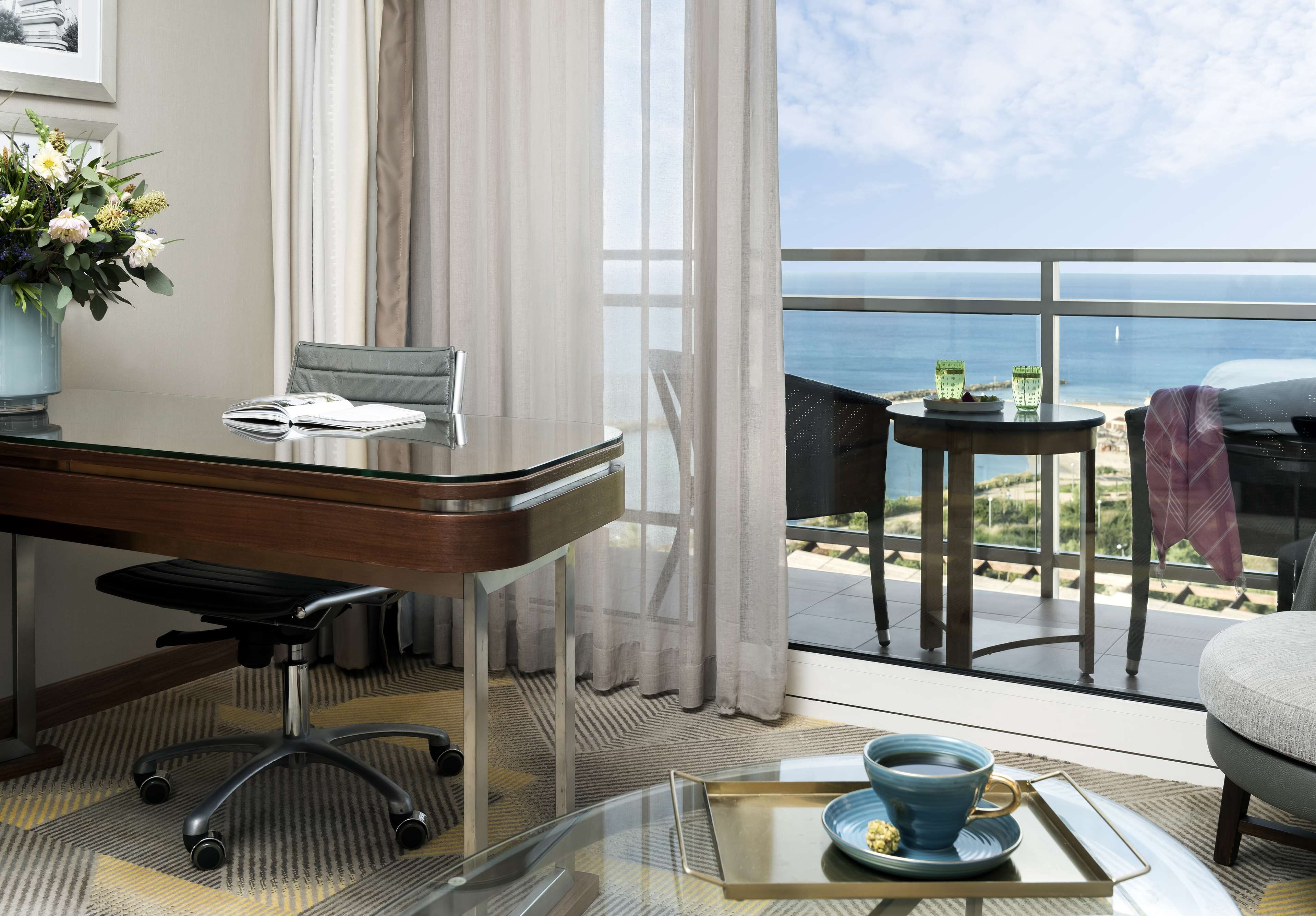 A hotel room with a desk, chair, and a view of the ocean.