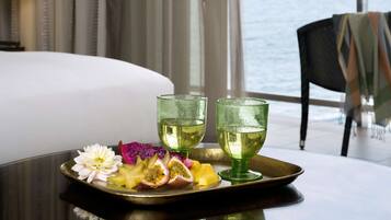 A tray with fruit and two glasses of a clear liquid on a table in a room with a view of the sea.