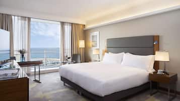 A hotel room with a large bed, a desk, a chair, and a view of the sea.