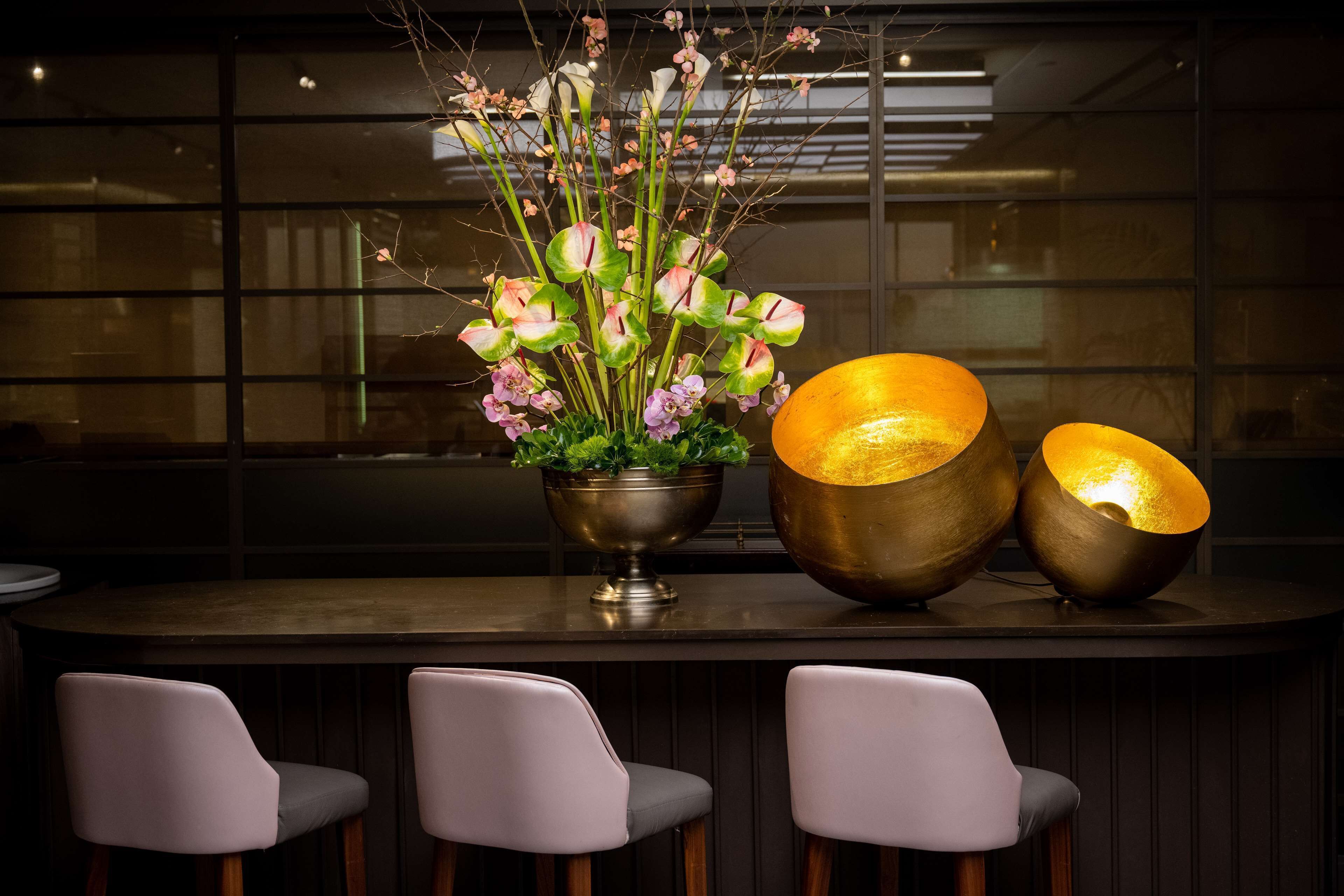 A bar area with three chairs, a large vase with flowers, and two illuminated lamps.