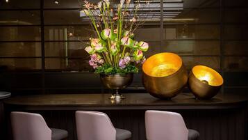 A bar area with three chairs, a large vase with flowers, and two illuminated lamps.