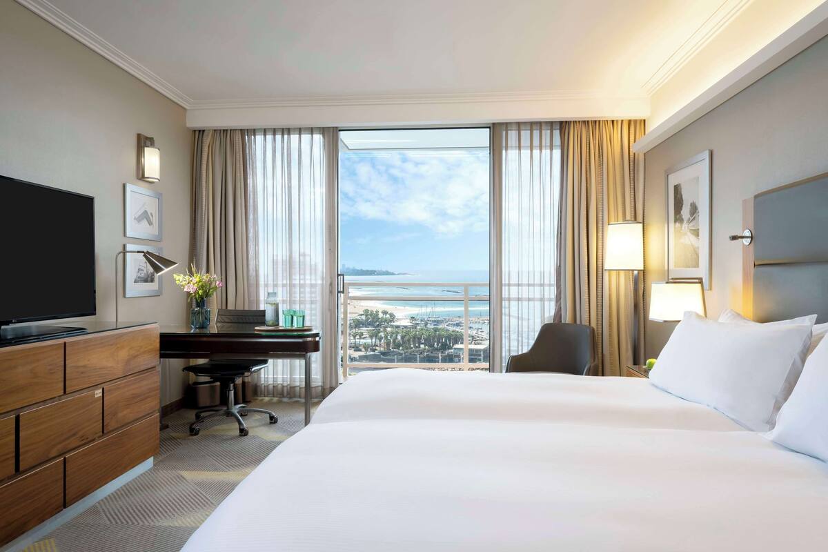 A hotel room with a large bed, a desk, a chair, a television, and a view of the ocean.