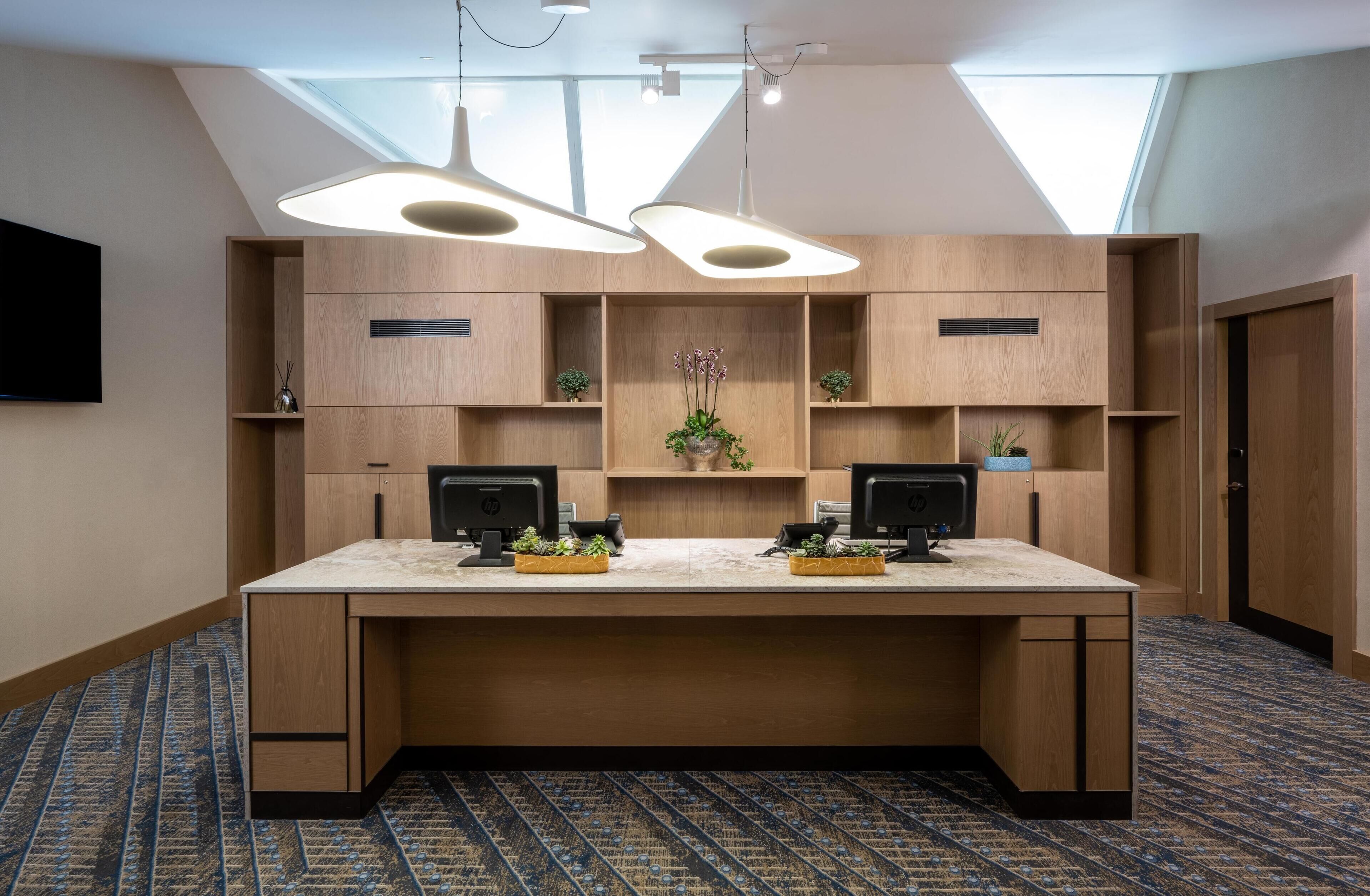 A modern office space with a large desk, two monitors, and a skylight.