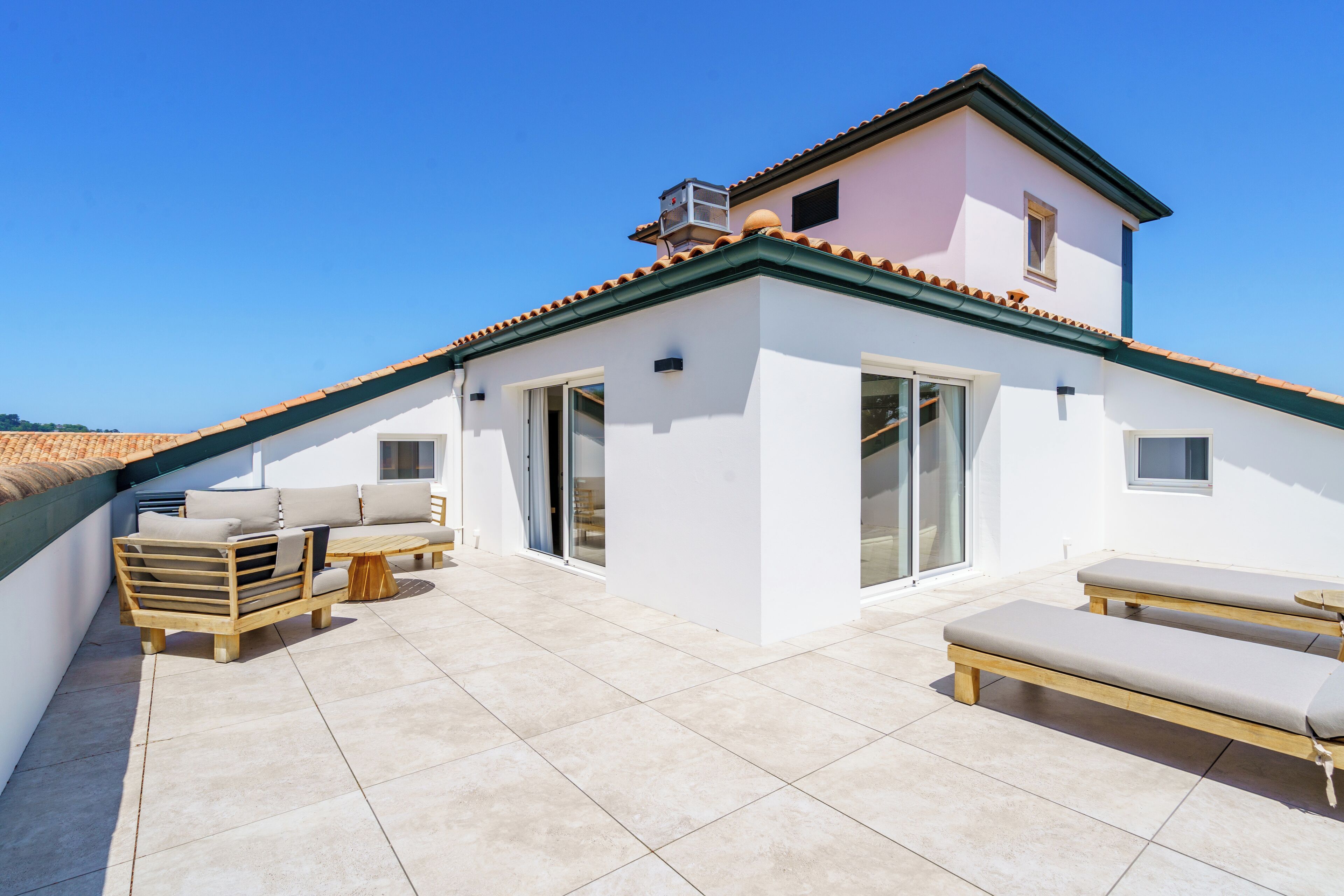 A rooftop terrace with a white building, a wooden deck, and two lounge chairs.