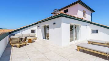 A rooftop terrace with a white building, a wooden deck, and two lounge chairs.