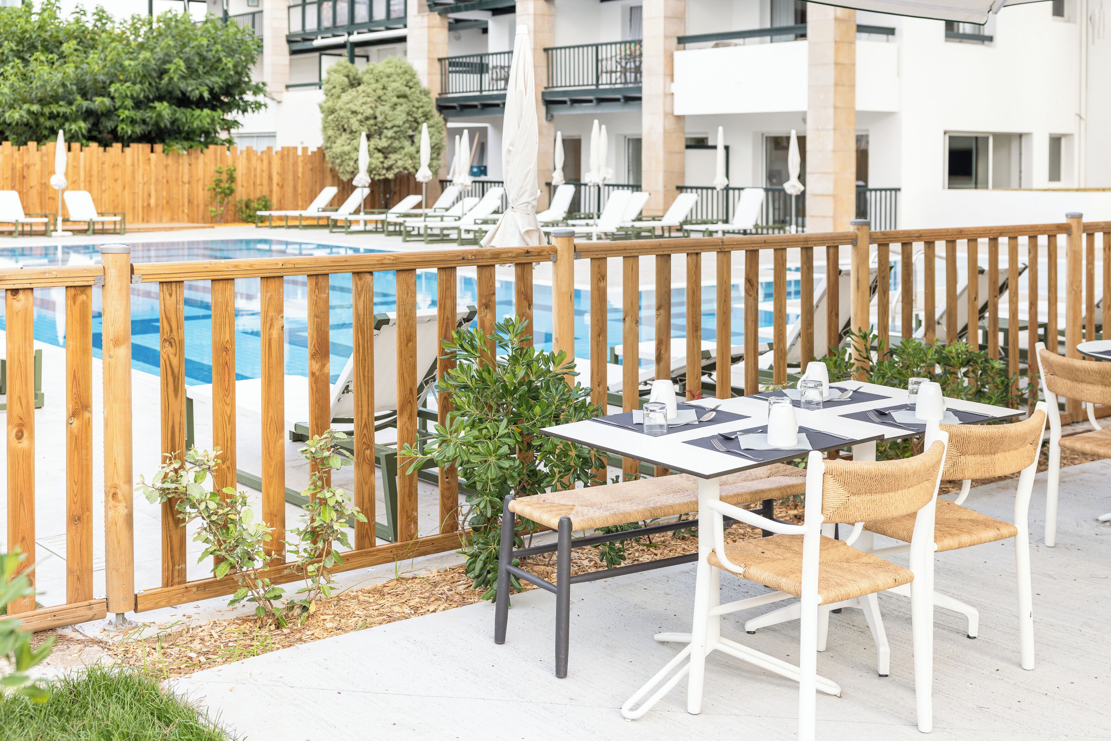 Zona junto a la piscina con valla de madera, sillas de descanso y una mesa con sillas.