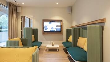 A modern hotel room with green upholstered sofas, a small white coffee table, and a television mounted on the wall.