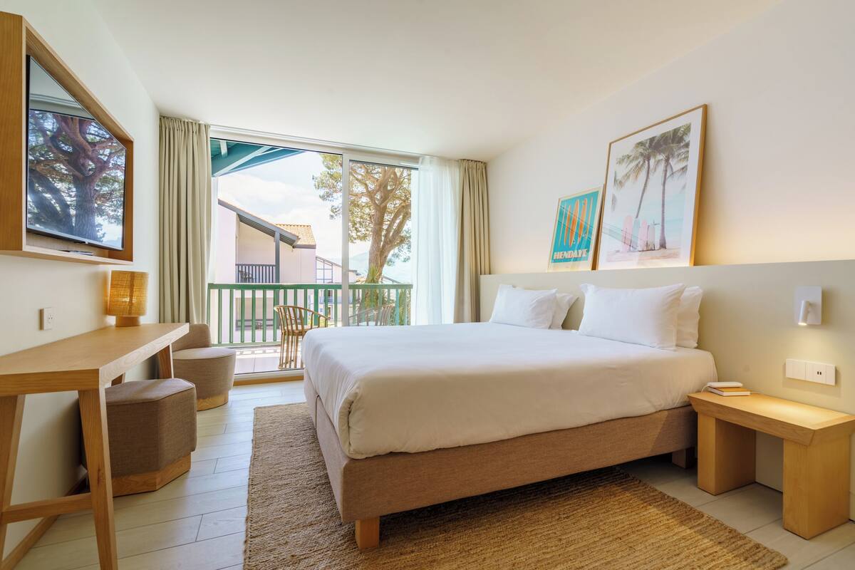 Habitación de hotel con cama, escritorio, silla, mesita y vistas al exterior.