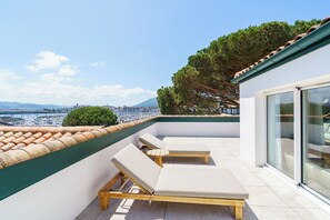 Una terraza en la azotea con dos tumbonas, vista al mar y una montaña al fondo.