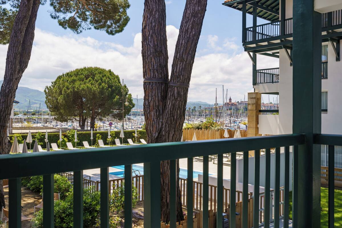 Un balcón con vistas a un puerto deportivo, árboles y una zona de piscina.