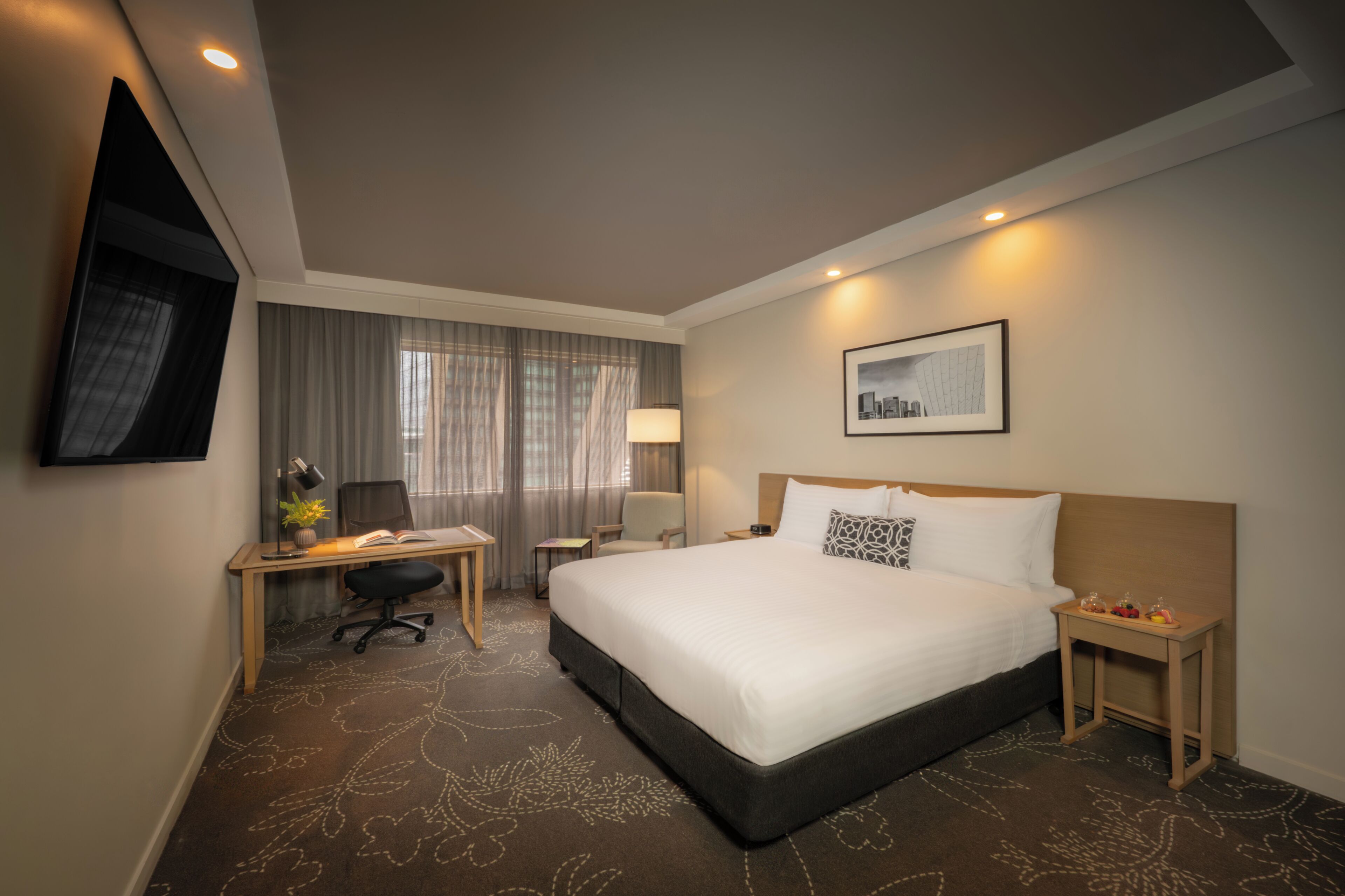 A hotel room with a bed, desk, chair, lamp, and a framed picture on the wall.