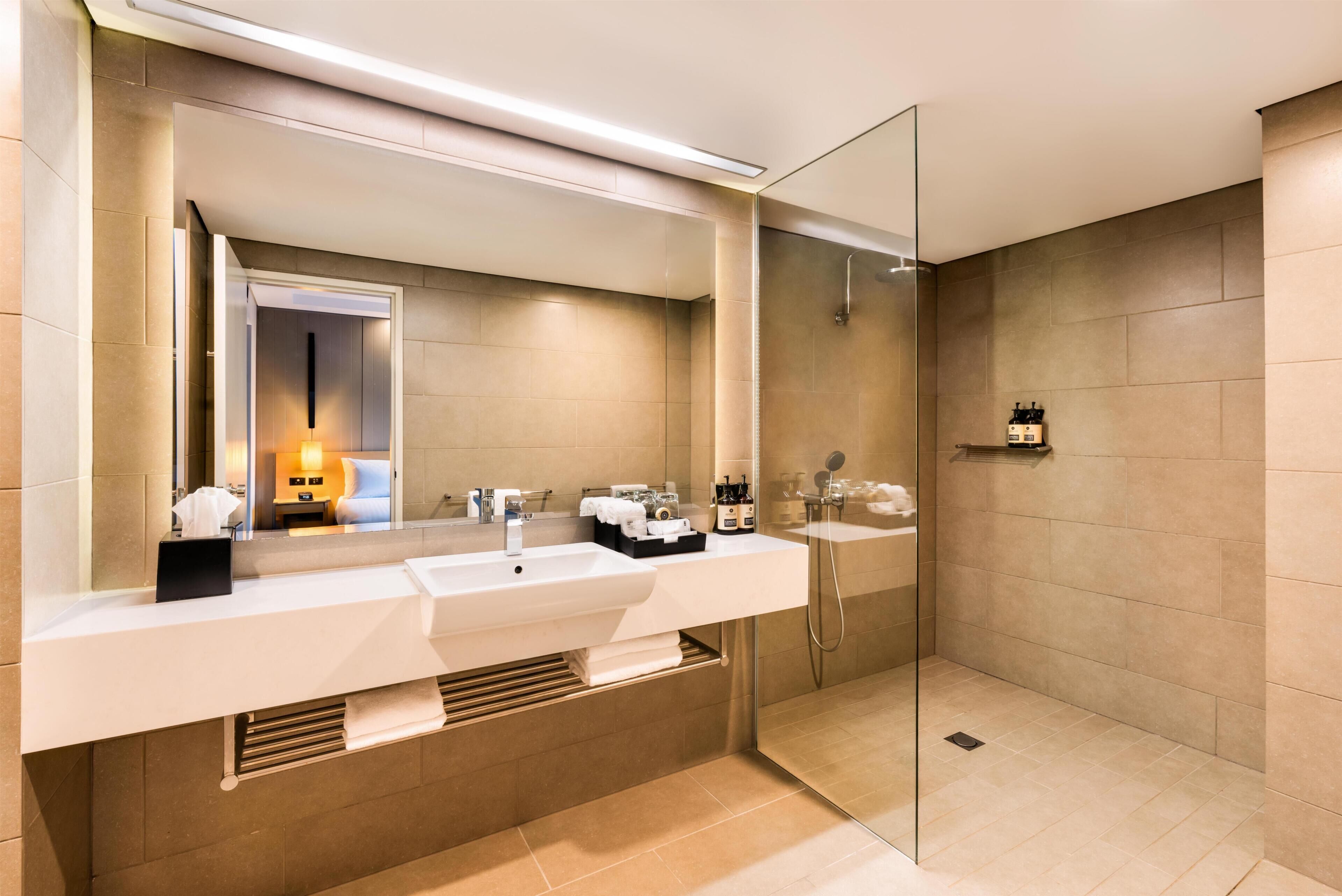 A modern bathroom with a large mirror, two sinks, a shower, and a towel rack.