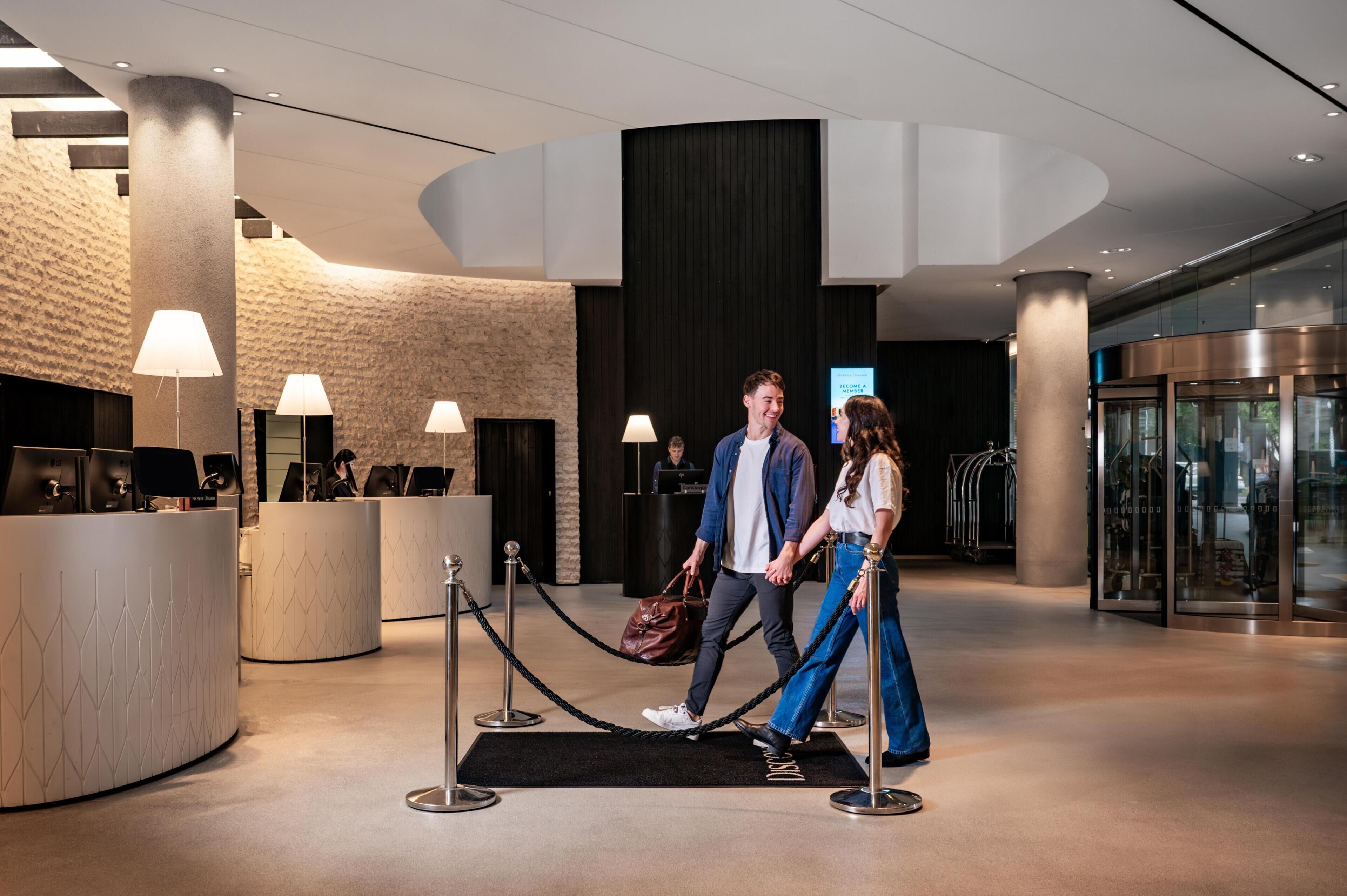 A modern hotel lobby with a reception desk, a black reception area, and a glass elevator.
