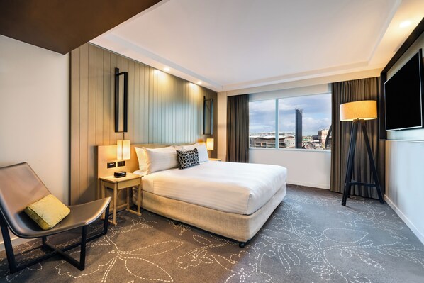 A hotel room with a bed, a chair, a nightstand, a lamp, a TV, and a view of the city. - PARKROYAL Darling Harbour, Sydney (Sydney)