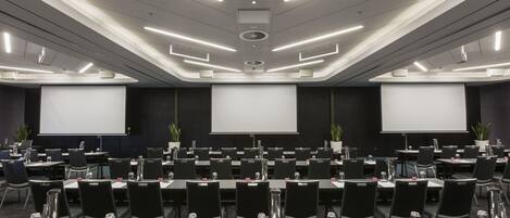 A conference room with rows of tables, chairs, and a large screen at the front.