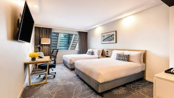 A hotel room with two beds, a desk with a chair, a TV mounted on the wall, and a window with curtains.