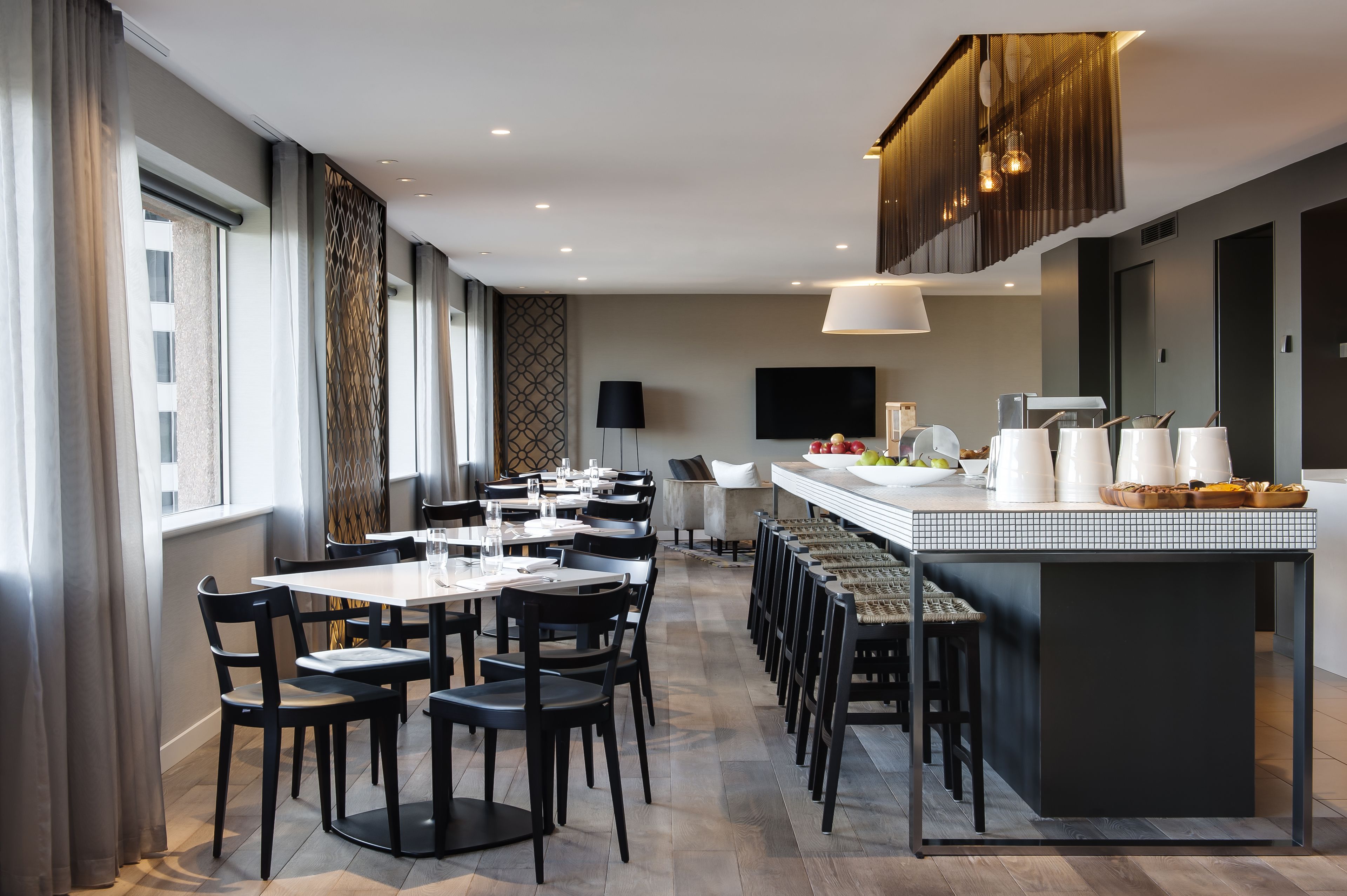 A modern dining area with a long counter, black chairs, and a television on the wall.