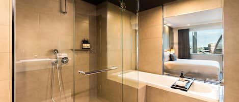 A modern bathroom with a glass-enclosed shower, a large mirror, and a view of a bed and cityscape through the window.