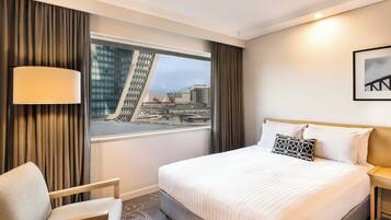 Habitación de hotel con una cama grande, una silla, un ventanal con vista a la ciudad y una lámpara.