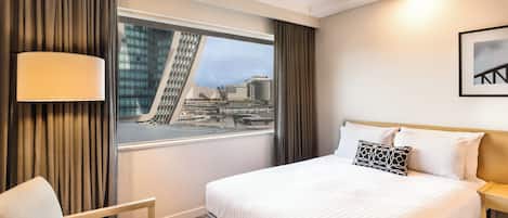Ein Hotelzimmer mit einem großen Bett, einem Sessel, einem Fenster mit Blick auf die Stadt und einer Lampe.