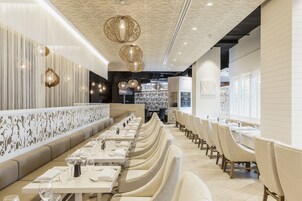 Un restaurante moderno con mesas largas y cabinas acolchadas, techo decorativo e iluminación colgante.