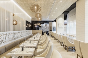 Un restaurante moderno con mesas largas y cabinas acolchadas, techo decorativo e iluminación colgante.