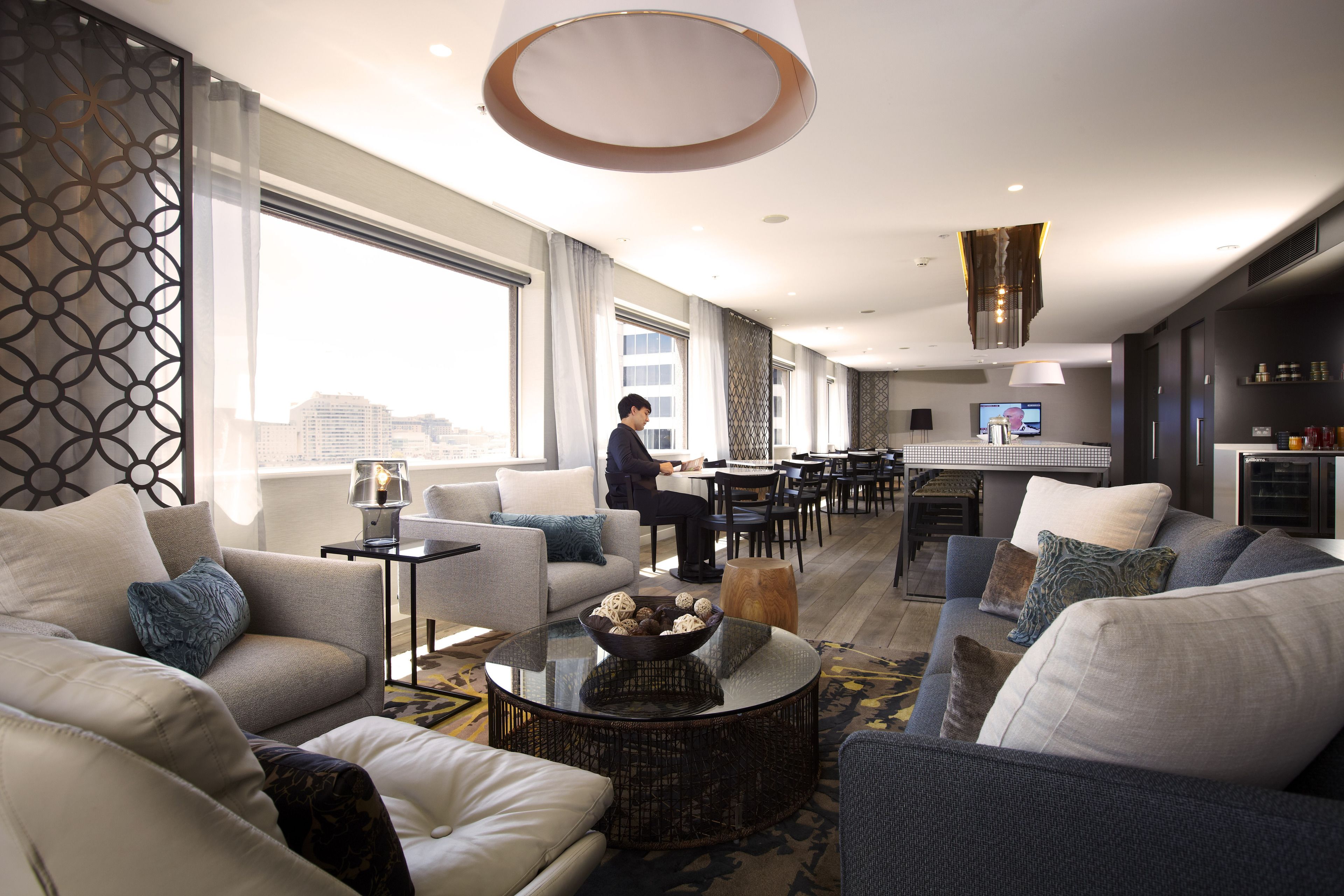 Et moderne hotelværelse med siddeområde, spisebord og stort vindue med byudsigt.
