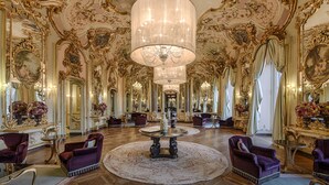 An opulent room with a grand chandelier, ornate gold detailing, and a large mirror reflecting the luxurious decor.