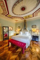 Una camera da letto lussuosa con un letto grande, una panca rossa, uno specchio e un soffitto decorato.