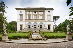 Un'imponente edificio simmetrico con una scalinata centrale, circondato da un giardino curato e da statue.