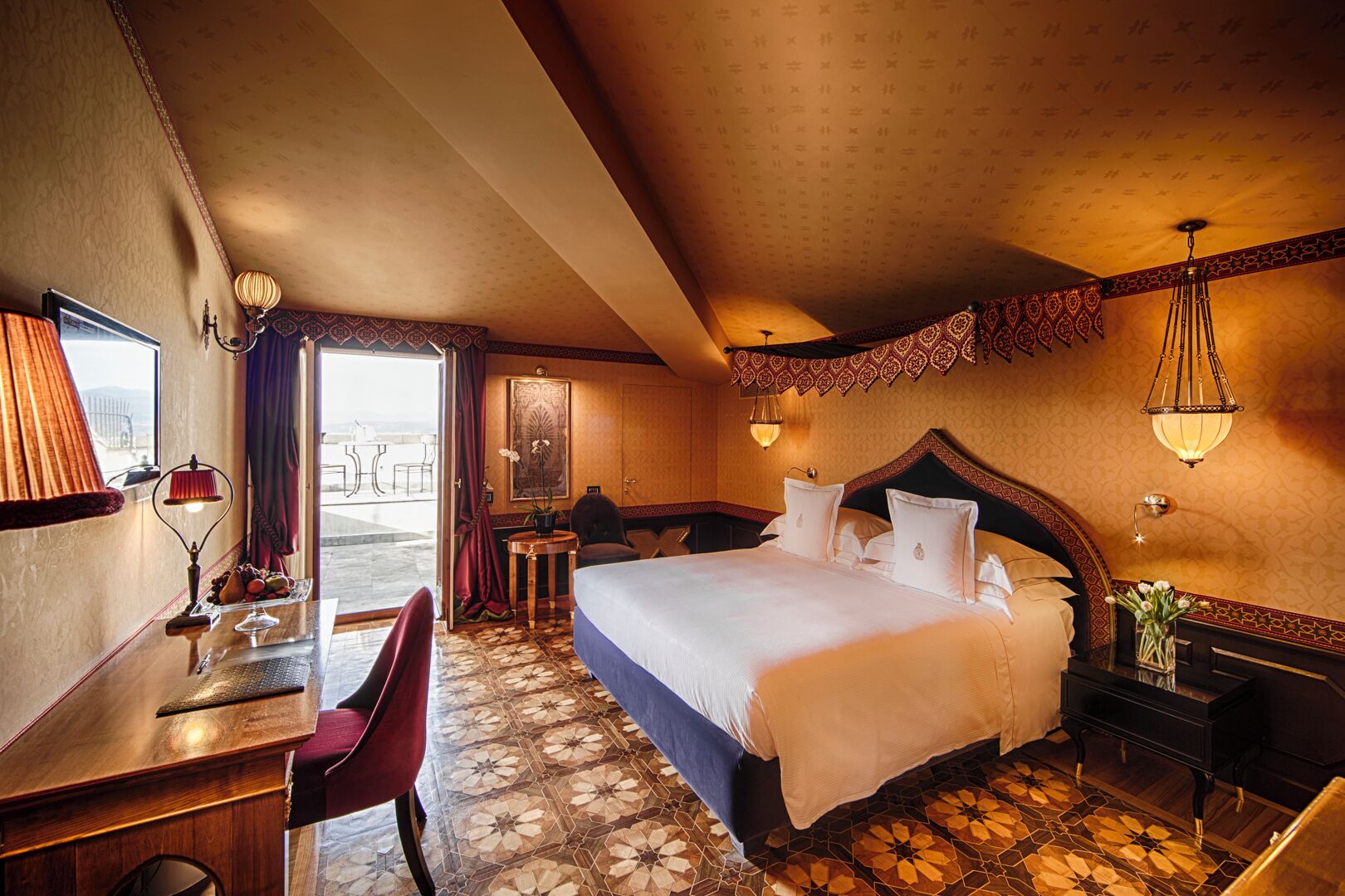 A hotel room with a bed, desk, chair, and a view of the outside.