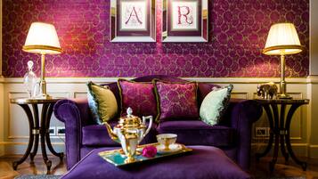 Um sofá roxo com almofadas decorativas, um tabuleiro com bule e xícaras, e duas molduras com as letras 'A' e 'R' na parede.